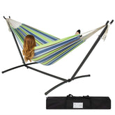 A woman sits comfortably in a hammock with a bag, surrounded by a serene outdoor setting.